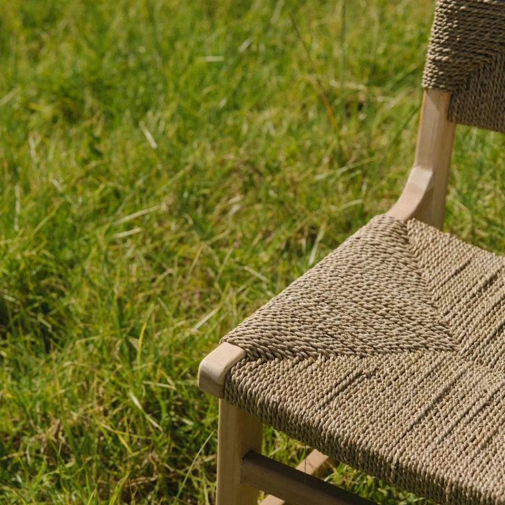 Cadeira em madeira teca e fibras naturais Juno Cadeira em madeira clara com assento e encosto trançados em fibra natural bege junto a relva verde