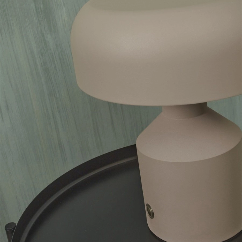 Candeeiro de Mesa em Metal Porto Lâmpada de mesa bege com base e cúpula arredondadas sobre superfície preta curva, parede verde clara