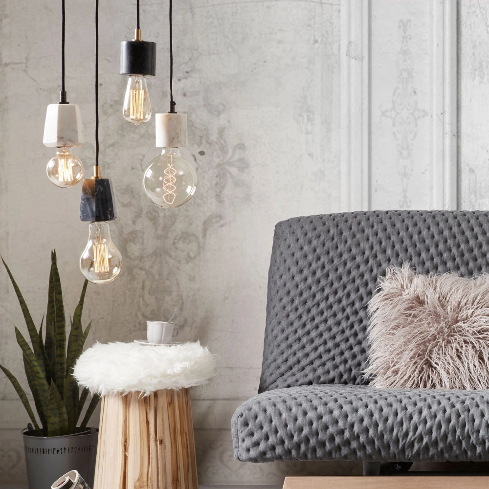 Candeeiro de Teto em Mármore Branco Brio Ø9x10 Sofá cinzento acolchoado, almofada felpuda, mesa de madeira com pelúcia branca, três lâmpadas pendentes e planta em vaso cinzento.
