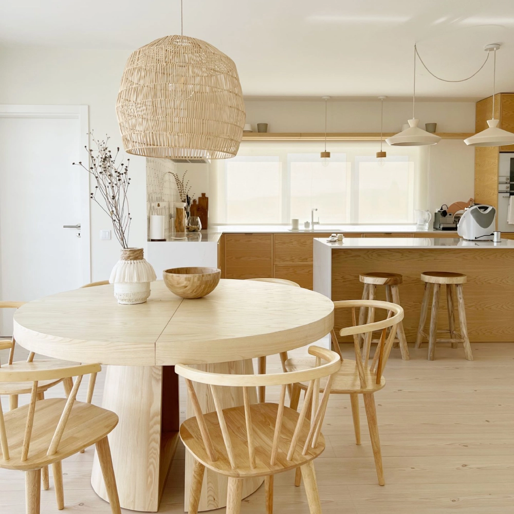 Candeeiro de Teto em Rattan Nama Ø60x52 Sala de refeições com mesa redonda e cadeiras de madeira clara, candeeiro pendente e cozinha em fundo com armários e balcão em madeira clara.