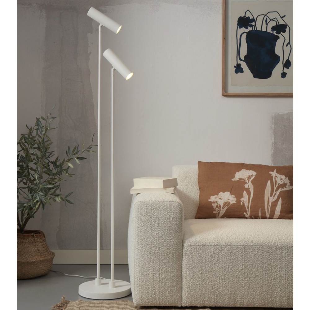 Candeeiro de Pé Havana com Duplo Foco Lâmpada de pé dupla branca junto a sofá branco com almofada castanha e planta em vaso