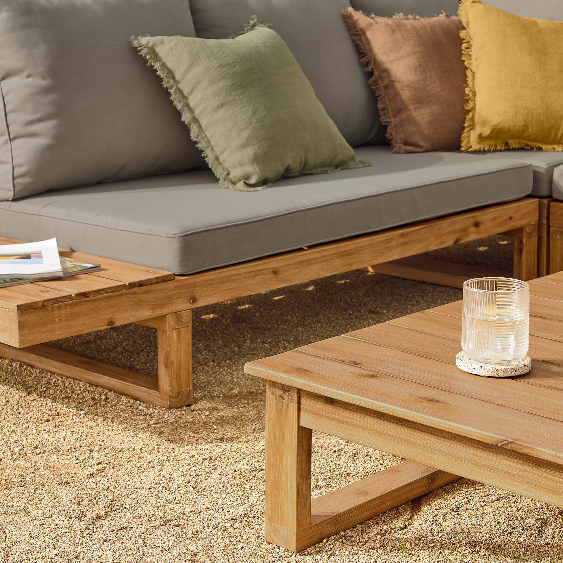 Conjunto Flavia, sofá 5 lugares, mesa, acácia Sofá em madeira clara com almofadas cinza e decorativas amarelas, verdes e castanhas e mesa de centro de madeira clara com vaso de vidro