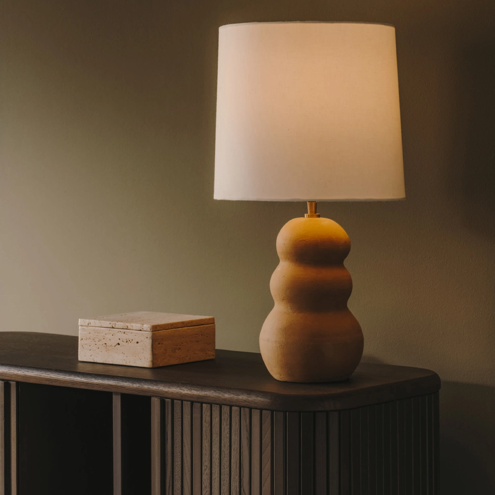 Candeeiro de Mesa em Terracota Maden Candeeiro de mesa com base ondulada castanha e aba branca sobre móvel de madeira escura