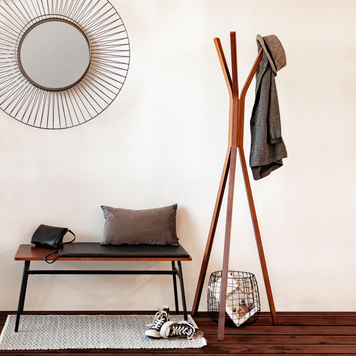 Cabide de pé Chelsi, nogueira, 170cm Banco de madeira com almofada, sapatos, cabide de madeira com casaco e chapéu e espelho redondo numa parede branca