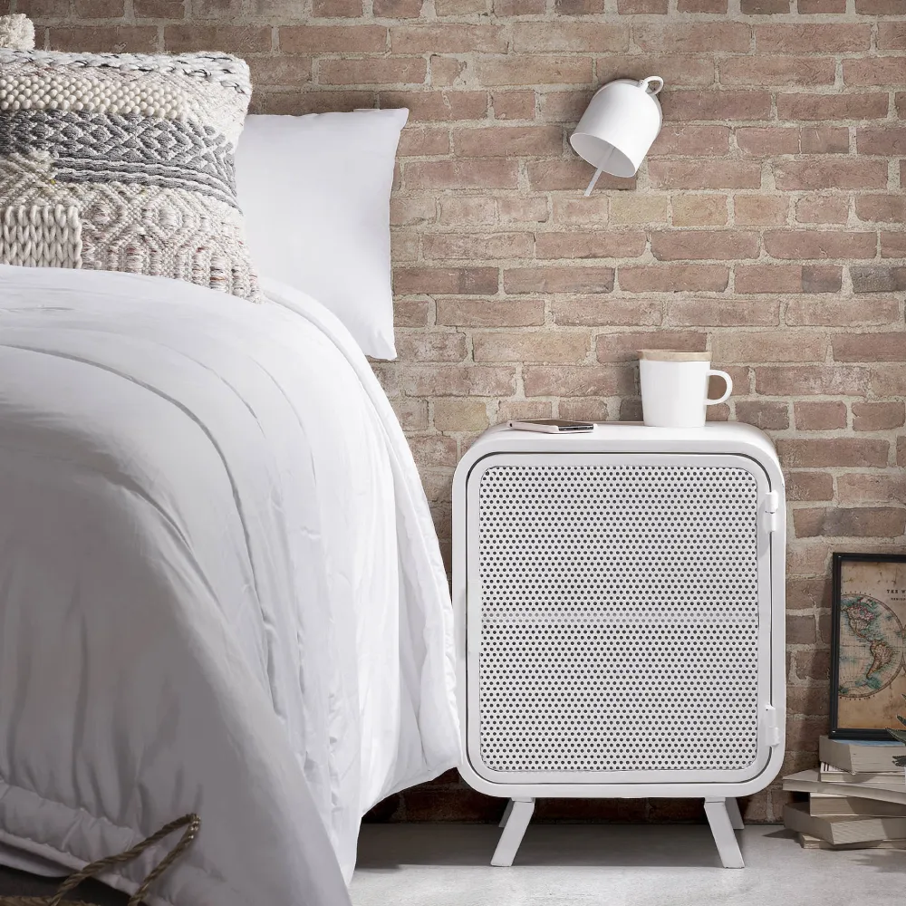 Aplique de Parede Regulável em Metal Lucy Quarto com cama branca, almofadas decorativas, parede de tijolos, mesa de cabeceira branca e luminária