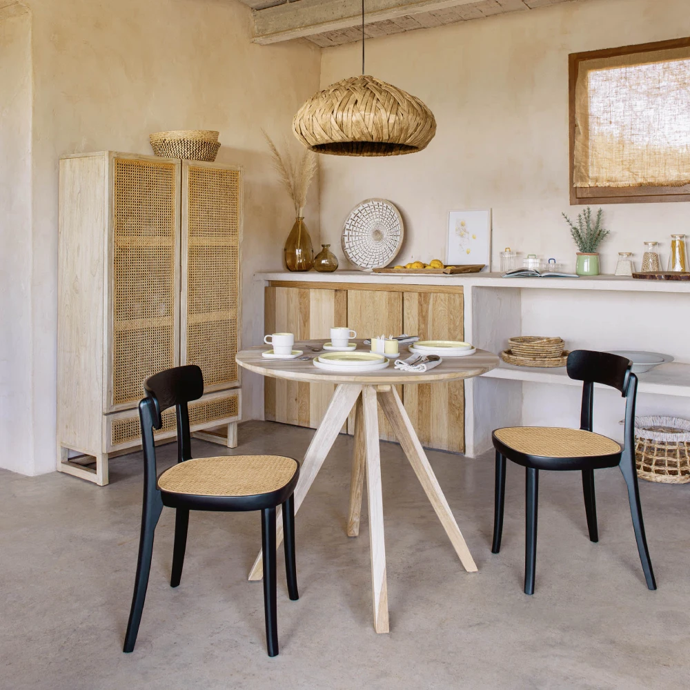 Cadeira em madeira faia com assento em rattan Roma Mesa redonda branca com duas cadeiras pretas de assento de palhinha num interior decorado com móveis de madeira clara e artigos de cerâmica