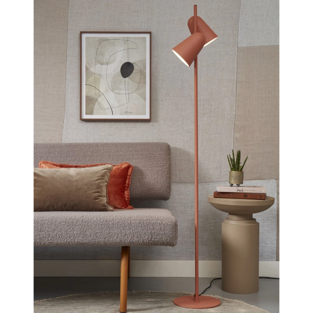 Candeeiro de Pé com Dois Focos Giratórios Salamanca Lâmpada de pé terracota com cabeças ajustáveis, sofá cinza, almofadas, mesa pequena bege, planta e quadro abstrato.