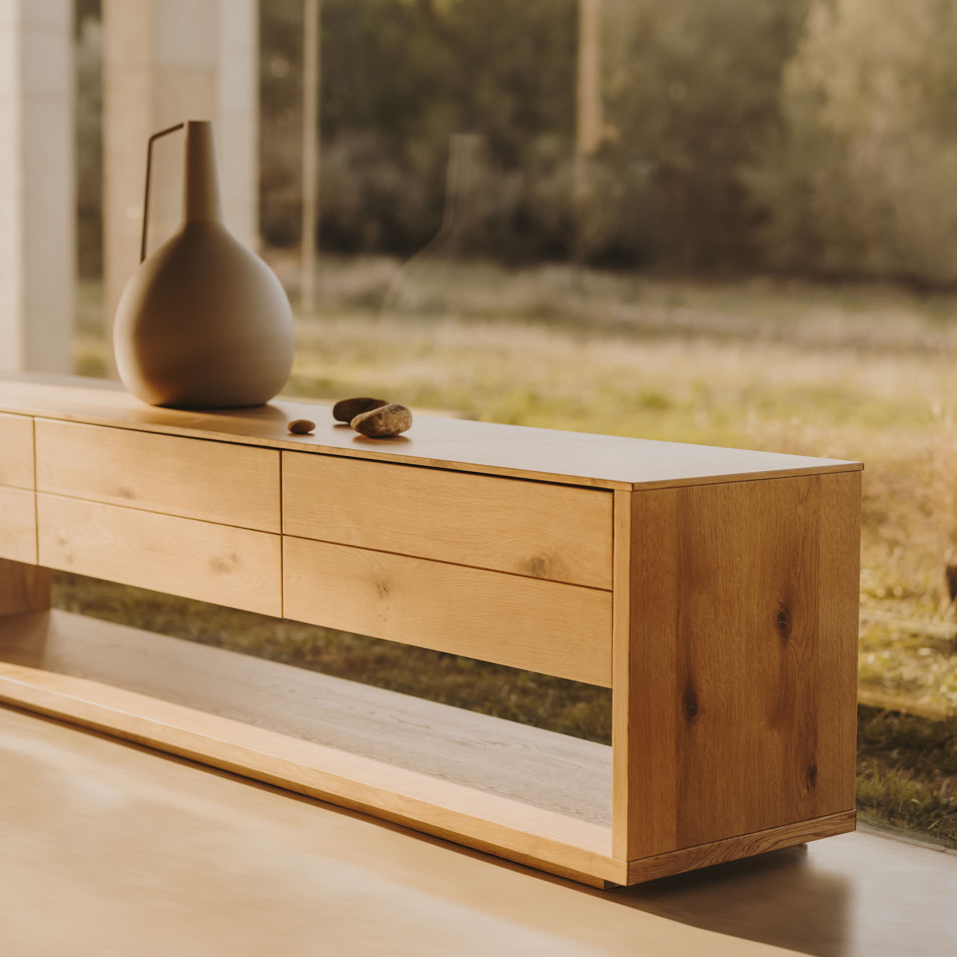 Móvel TV Alguam, madeira carvalho, 200x50 Móvel baixo em madeira clara com vaso decorativo cinzento no topo junto a uma janela grande