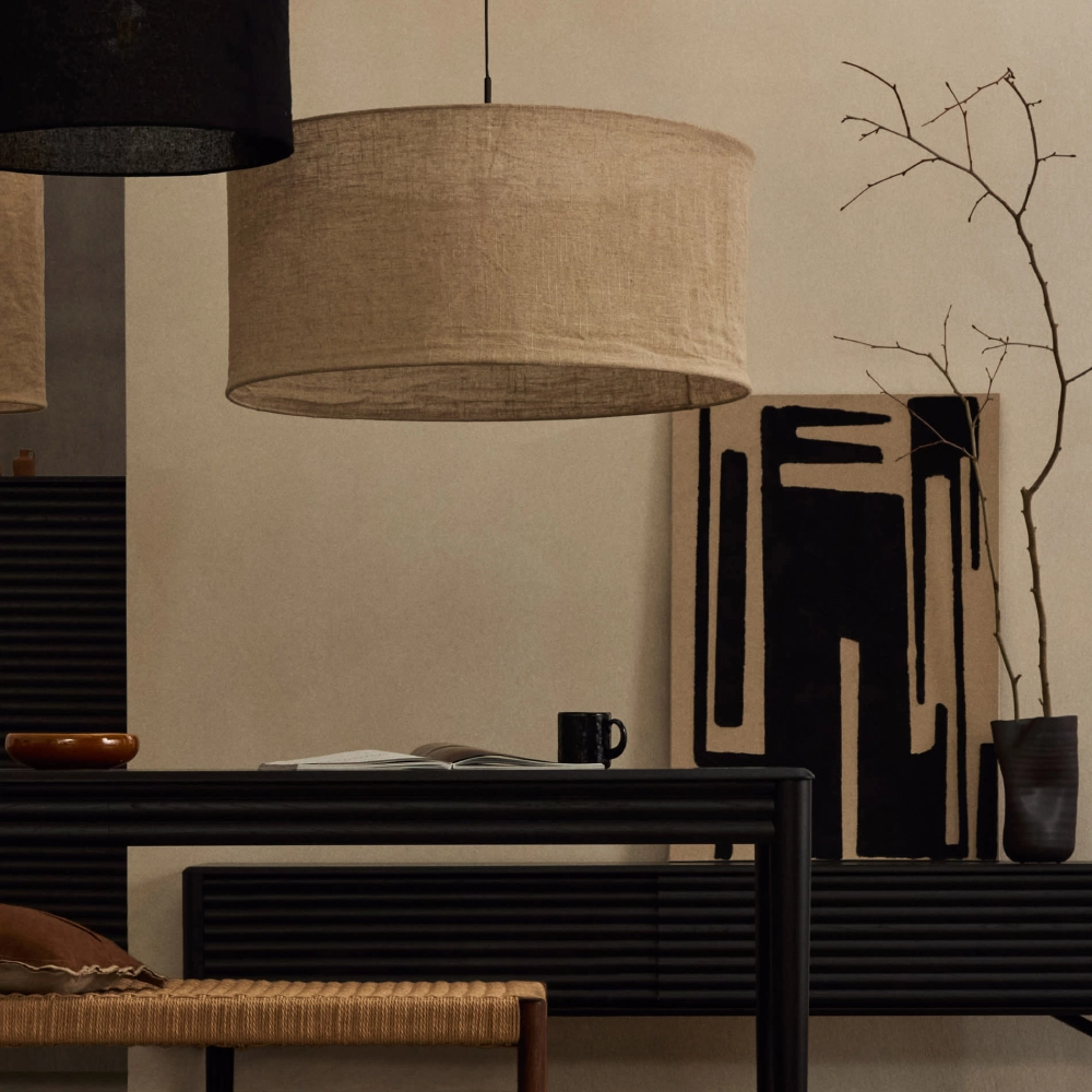 Candeeiro de Teto em Linho Marila Ø80x40 Abajur suspenso tecido bege sobre mesa preta com caneca e livro, quadro abstrato preto e bege, vaso com galhos secos