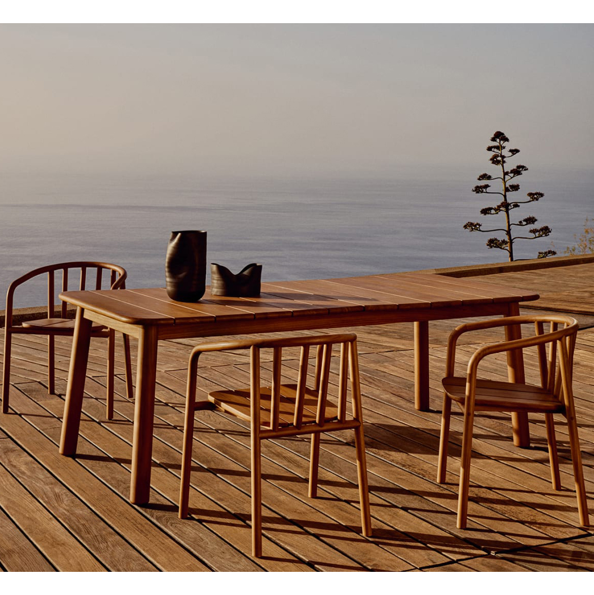 Cadeira Turquet, exterior, madeira teca Conjunto de mesa e quatro cadeiras de madeira num deck de madeira com vista para o mar ao pôr do sol