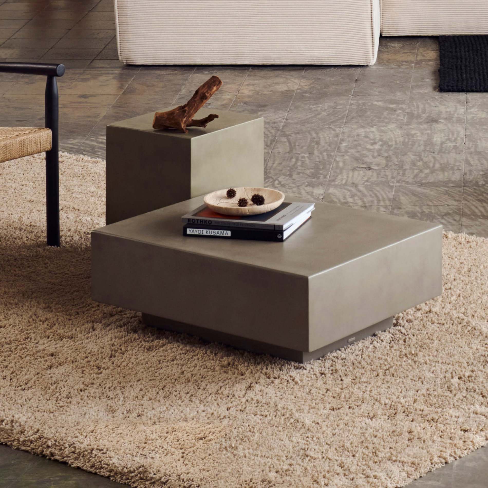 Mesa de centro Rustta, exterior, cimento, 80x60 Mesa de centro cúbica cinza com livros e prato sobre tapete bege