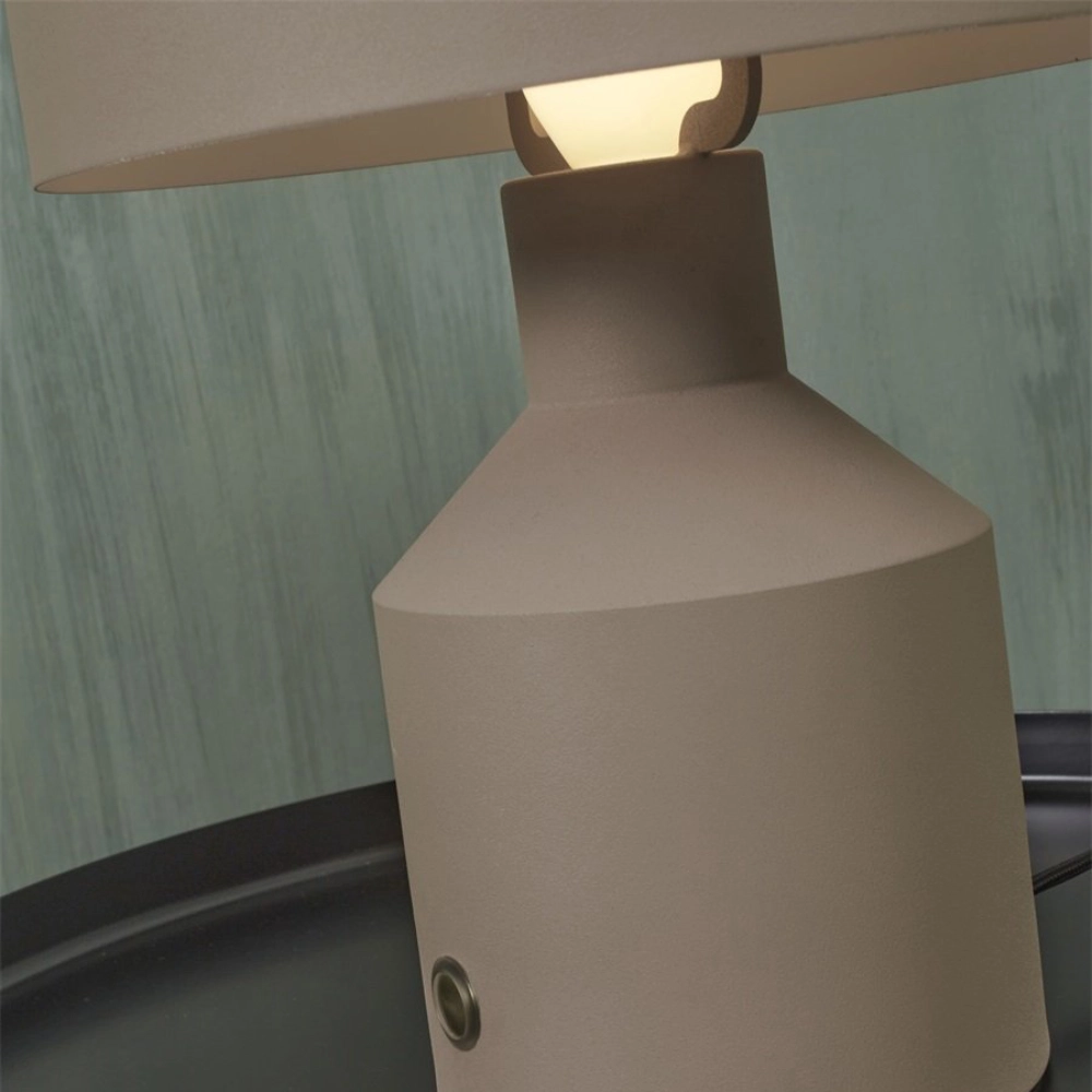 Candeeiro de Mesa em Metal Porto Abajur de mesa bege com cúpula clara ligado e superfície preta em fundo de parede verde água.