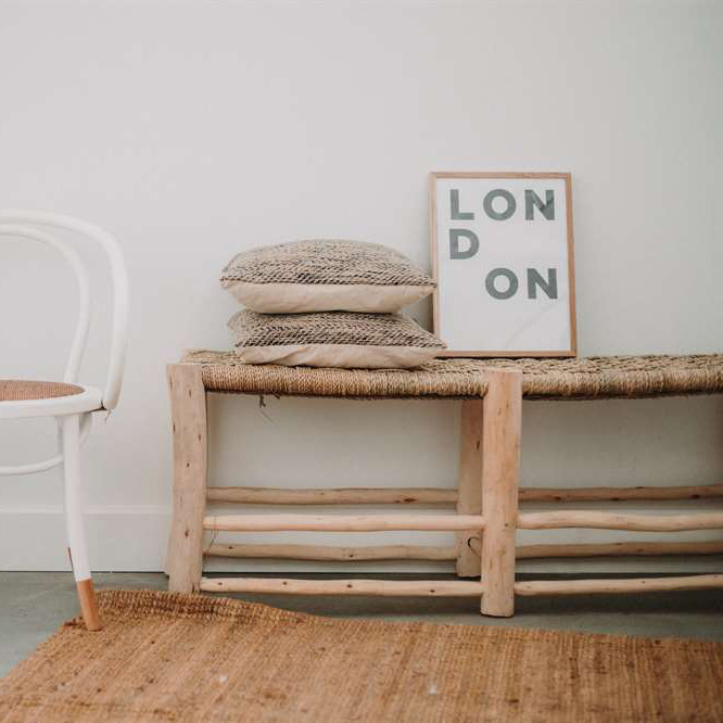 Banco Belgiu, madeira de eucalipto, 136x50 Banco rústico com almofadas e quadro com texto LONDON, ao lado de cadeira branca e tapete natural