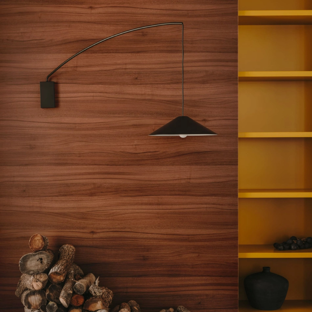 Aplique de Parede Giratório Kali Lâmpada suspensa preta sobre parede de madeira com estante amarela ao lado e troncos no chão