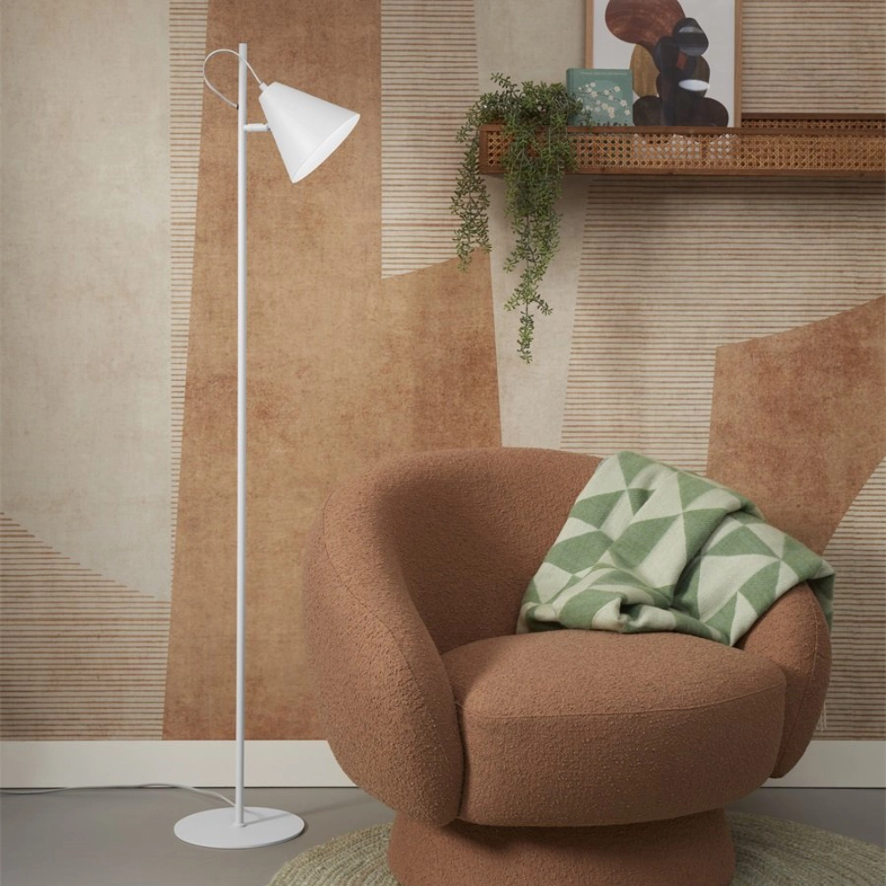 Candeeiro de Pé Articulado em Metal Lisbon Lâmpada de pé branca junto a poltrona castanha com manta verde e branca, prateleira em rattan com planta e quadro