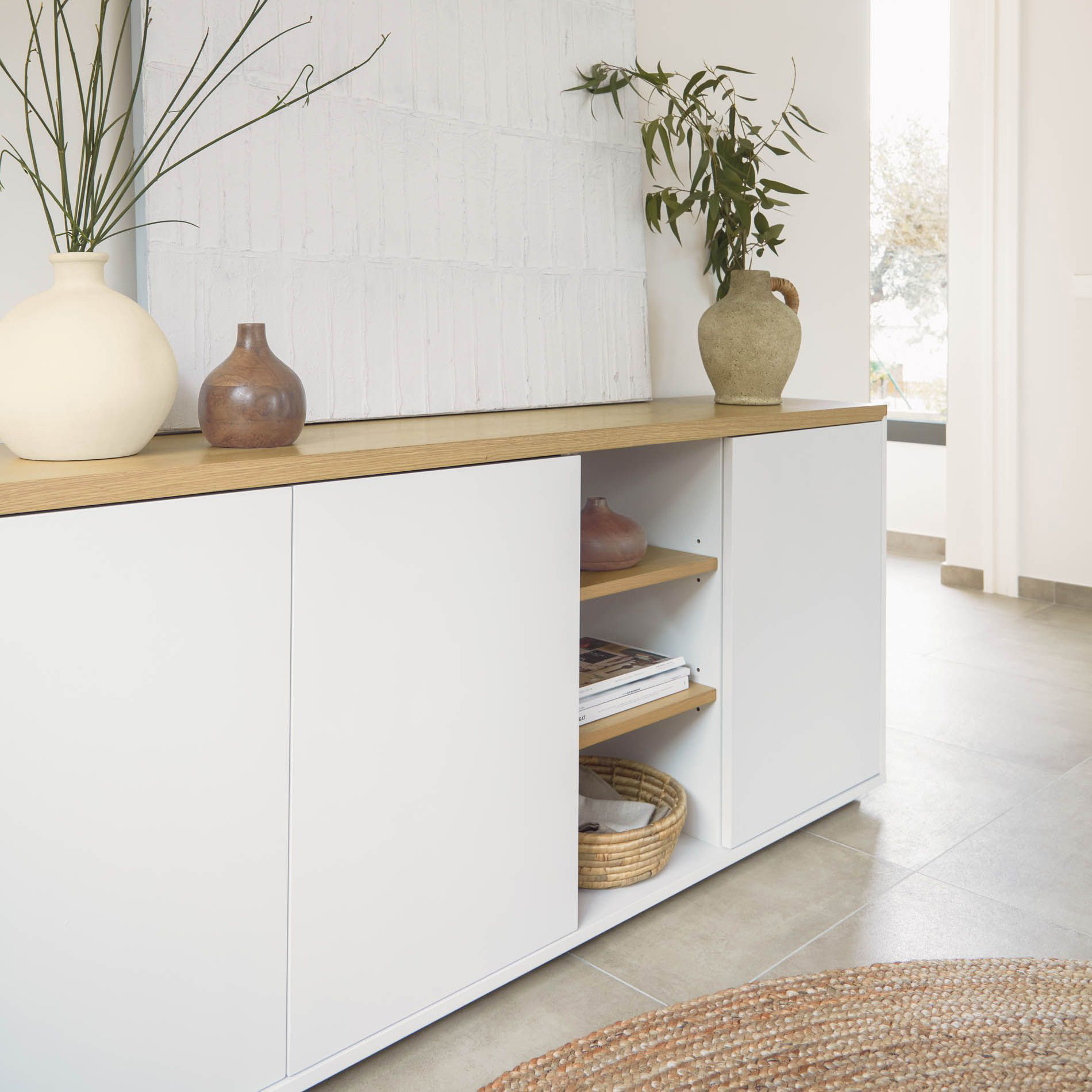 Aparador Abil, carvalho/lacado, 180x75 Móvel branco com tampo em madeira clara decorado com vasos de cerâmica e folhas verdes num ambiente minimalista.