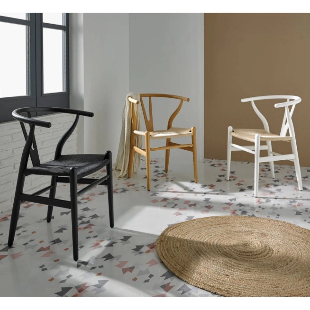 Cadeira com braços em madeira faia Wishbone Três cadeiras de madeira com palhinha em cores preta, castanha e branca em piso geométrico com tapete redondo
