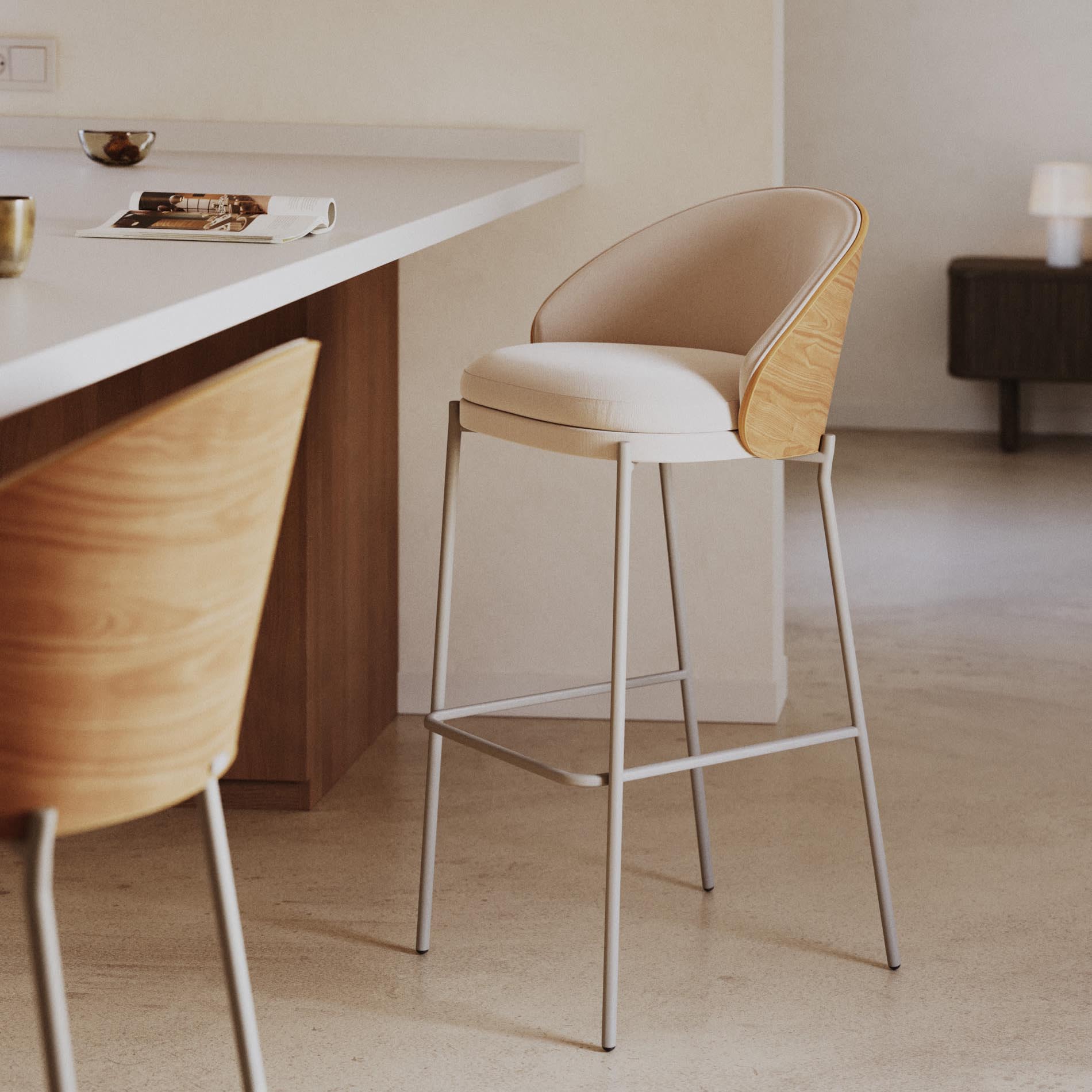 Cadeira alta Emmy, estofada, madeira, bege, 77cm Cadeira alta de bar com estrutura madeira e assento bege junto a balcão branco