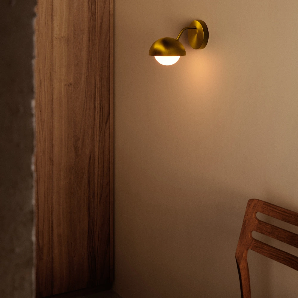 Aplique de Parede em Metal Dourado Lola Lâmpada de parede dourada acesa junto a cadeira de madeira contra parede bege