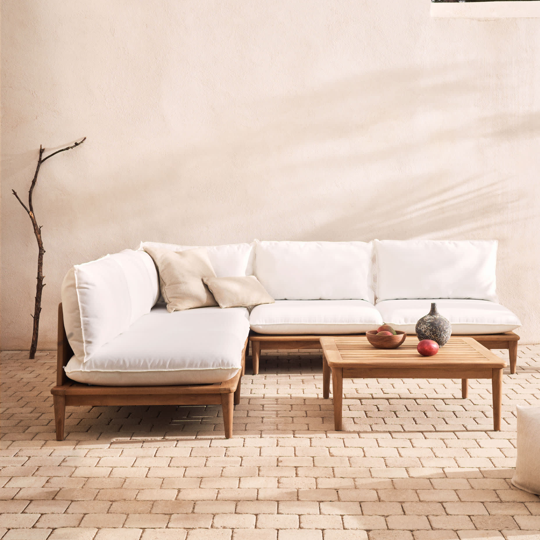 Conjunto Porto Rico, sofá 4 lugares, mesa, madeira teca Sofá em L branco com estrutura de madeira e mesa de centro de madeira num ambiente de pavimento de pedras e parede bege