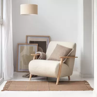 Poltrona creme com braços de madeira e almofada cinza num ambiente minimalista