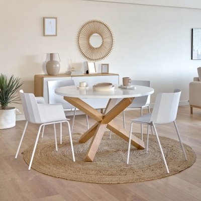 Mesa de jantar redonda branca com base de madeira e quatro cadeiras brancas num tapete redondo de ráfia