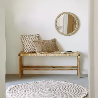 Banco de madeira com almofadas e espelho redondo numa parede branca com tapete redondo branco no chão