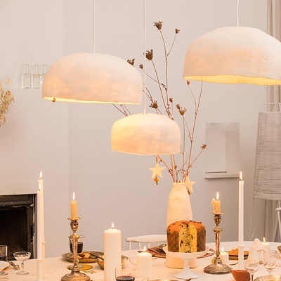 Candeeiros de teto bege, velas em castiçais dourados, bolo e vaso com ramos secos num ambiente interior