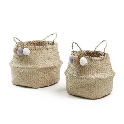 Dois cestos de palha com pompons e alças sobre fundo branco