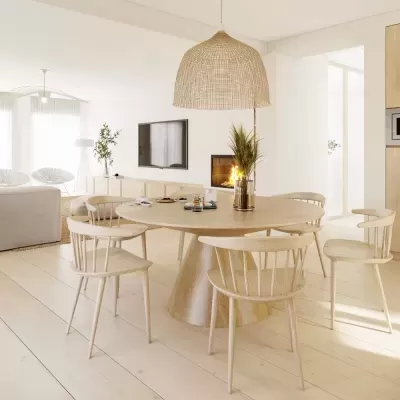 Mesa oval de madeira clara com seis cadeiras combinando e luminária suspensa em sala iluminada