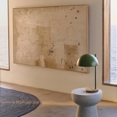 Sala com mesa de pedra, candeeiro verde, tapete azul e quadro abstrato bege com vista para o mar