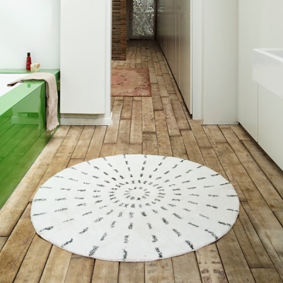 Tapete redondo branco com padrão preto em espiral numa casa de banho com chão de madeira e banheira verde
