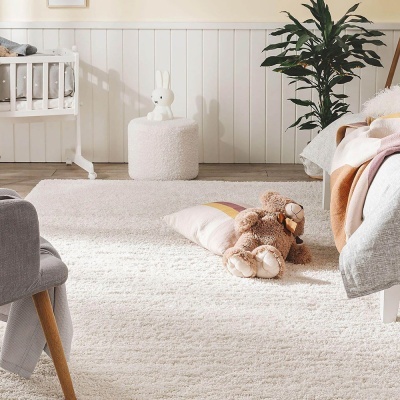 Quarto infantil com tapete branco, peluche, almofada, pufe, berço e planta