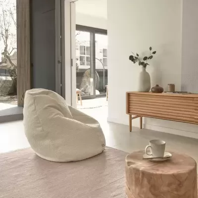 Cadeira pufe branca em tecido macio numa sala clara com móvel de madeira e copo com chávena