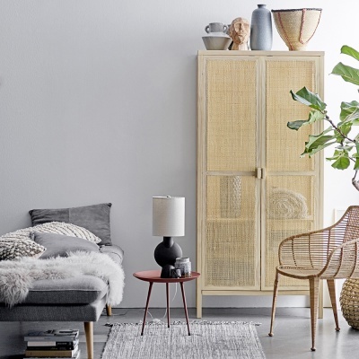 Sala de estar com sofá cinza, mesa vermelha, armário de madeira clara com palha e cadeira de vime