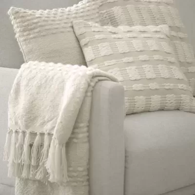 Sofá cinzento claro com almofadas e manta texturizadas em tons neutros