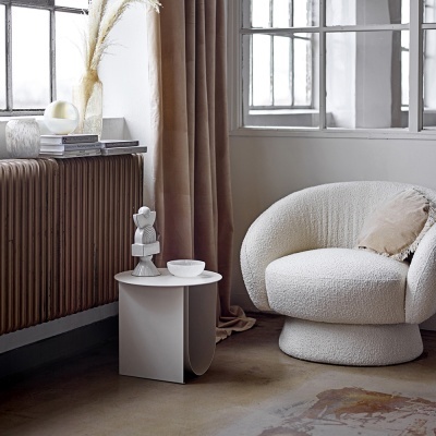 Poltrona branca bouclé com mesa lateral branca e cortina castanha numa sala com janela