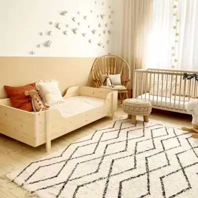 Quarto infantil com cama de madeira, berço, tapete geométrico, cadeira de vime e decoração de pássaros
