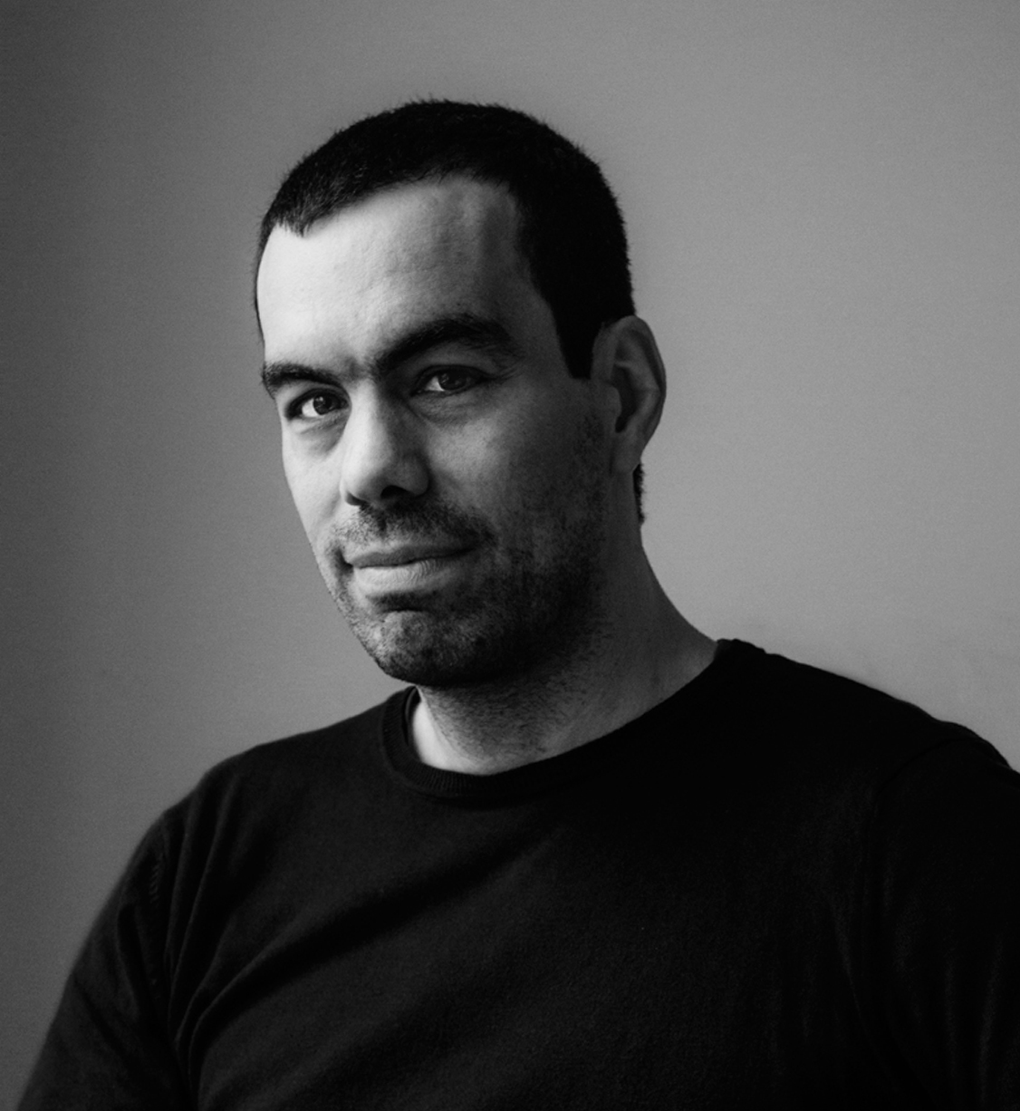 Homem com t-shirt preta num retrato a preto e branco com fundo cinza