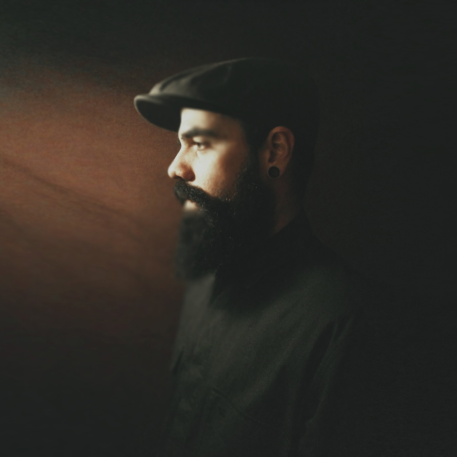 Homem com boina preta e barba espessa em fundo escuro
