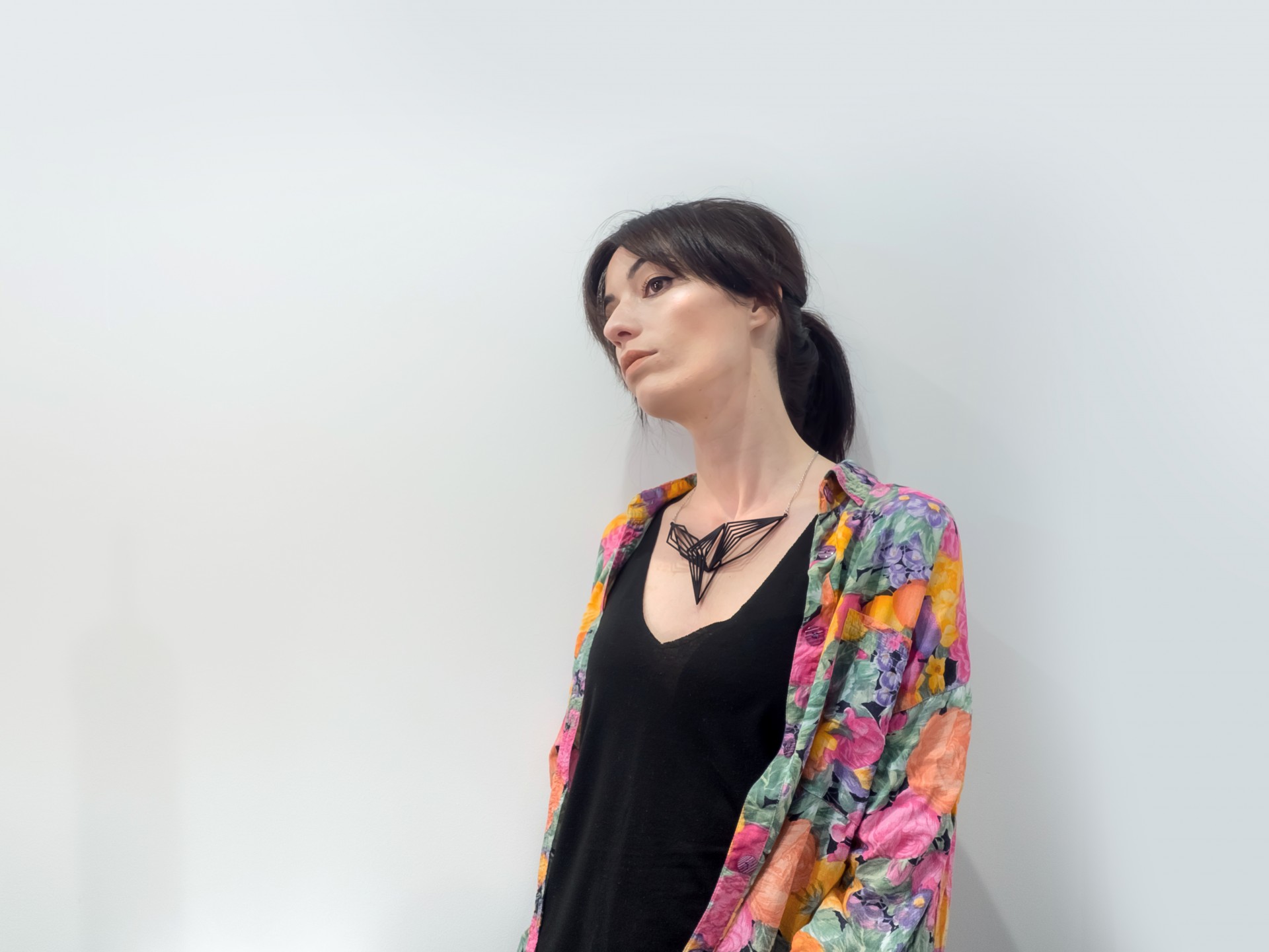 Mulher com camisa floral colorida e colar preto sobre fundo branco