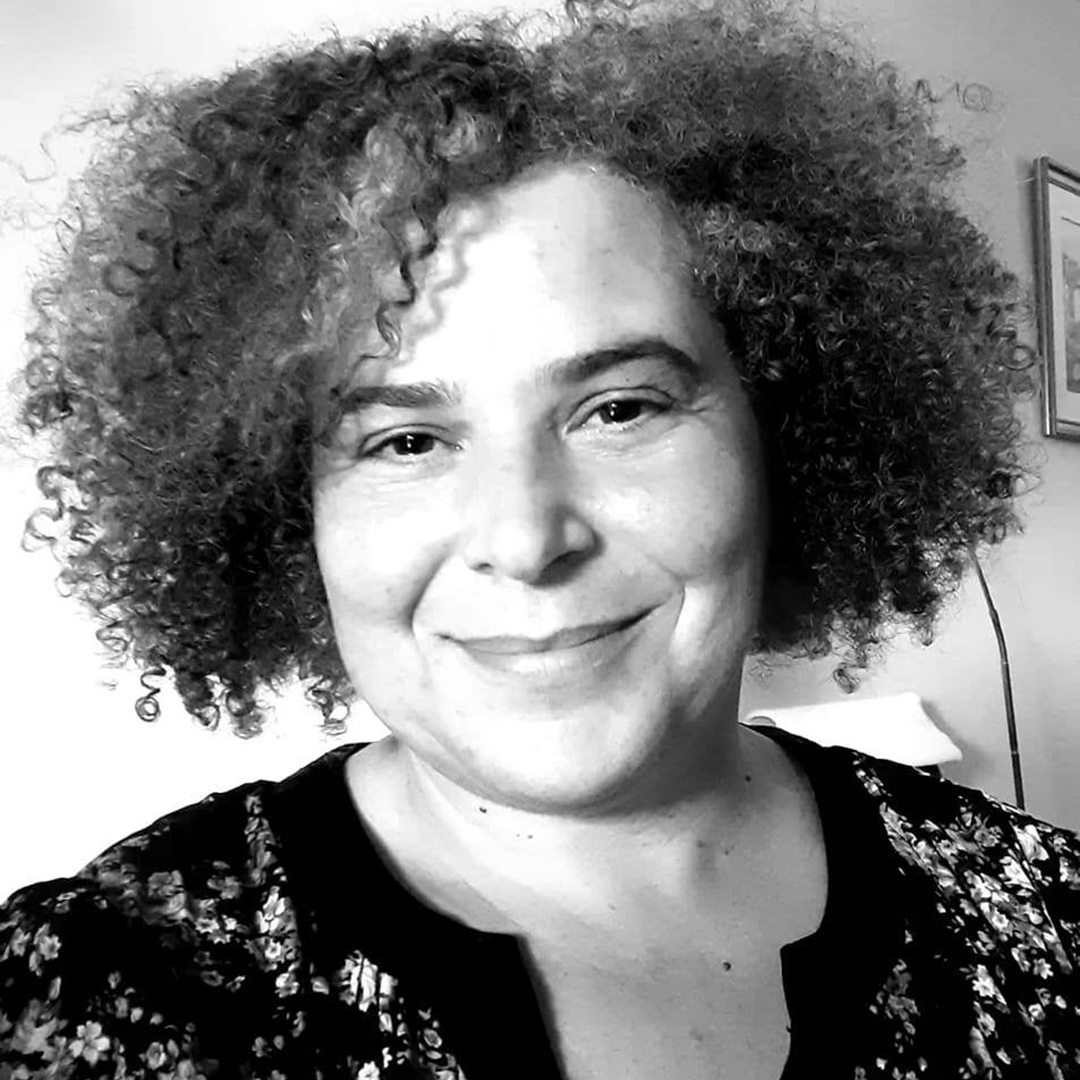 Retrato de mulher sorridente com cabelo encaracolado e curto, vestindo camisa floral.