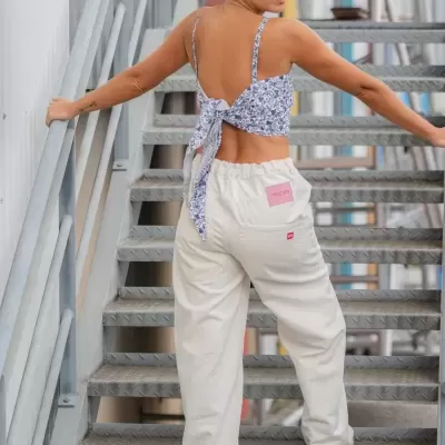 Mulher com top floral azul e calças brancas largas numa escada metálica cinza