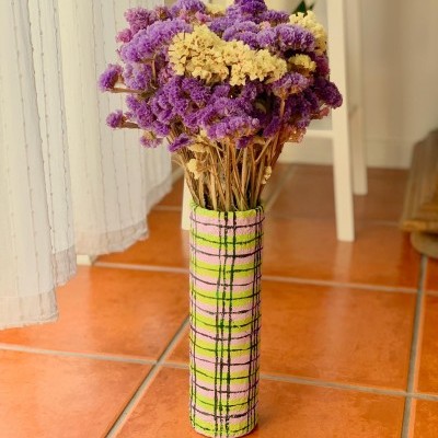 Vaso decorativo de padrão xadrez com flores secas roxas e amarelas em chão de azulejos terra-cota