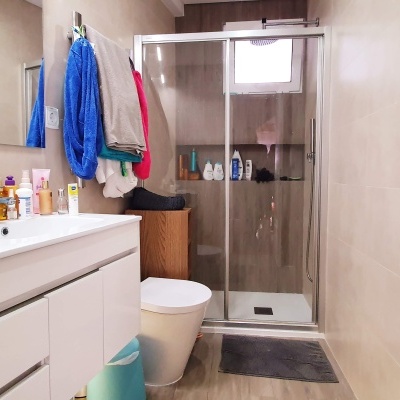 Casa de banho com lavatório branco, sanita, chuveiro com porta de vidro e azulejos beje