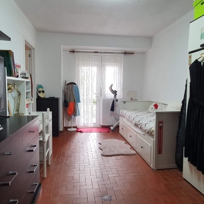 Quarto estreito com cama branca, guarda-roupa branco e cómoda castanho escuro com TV