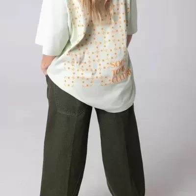 Pessoa de costas com t-shirt branca com padrão laranja e calças largas verde-escuras