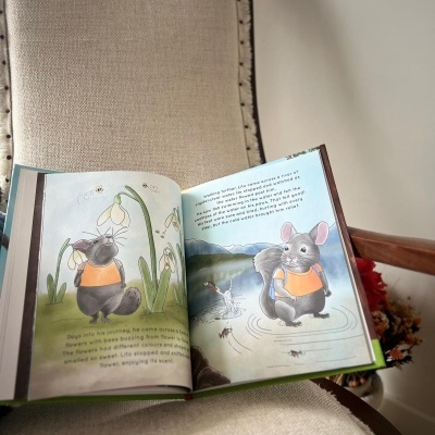 Livro infantil aberto com ilustrações de rato cinzento e texto em inglês numa cadeira estofada creme
