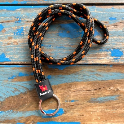 Chaveiro com cordão preto e laranja, anel metálico e etiqueta Fonsica sobre madeira azul
