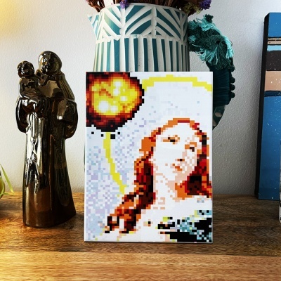 Quadro pixelado de mulher com cabelo ruivo num ambiente com estatueta dourada e vaso decorativo